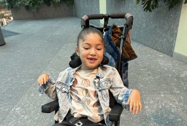 In this photo, a girl named Raquel poses from her wheelchair with a smile. To help her and others, consider launching a campaign to raise funds for research on mitochondrial disease.